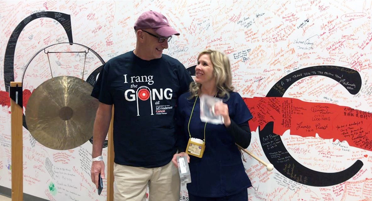 2017年11月3日，Rob Gales和放射治疗师Denice Jones一起站在质子治疗中心的锣旁，庆祝他的治疗结束