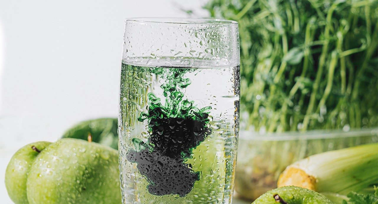 一杯含有叶绿素的水。后面是绿色的水果和蔬菜。