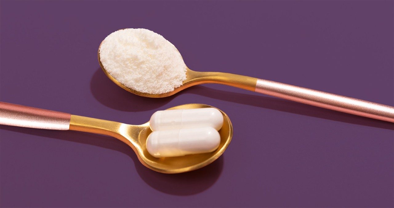 在紫色背景的两个金匙子，一个有白色粉末和一个与白色胶囊药片