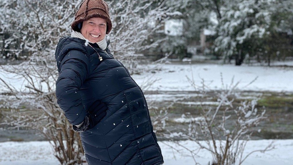 三阴性炎性乳腺癌幸存者亚历山德拉·兰德穿着她的冬衣和帽子在雪地里露出她怀孕的肚子