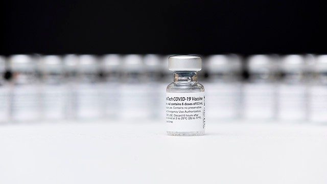 清晰的瓶COVID-19疫苗联合起来反对一个黑色背景,与一个瓶在其他人面前坐在中间