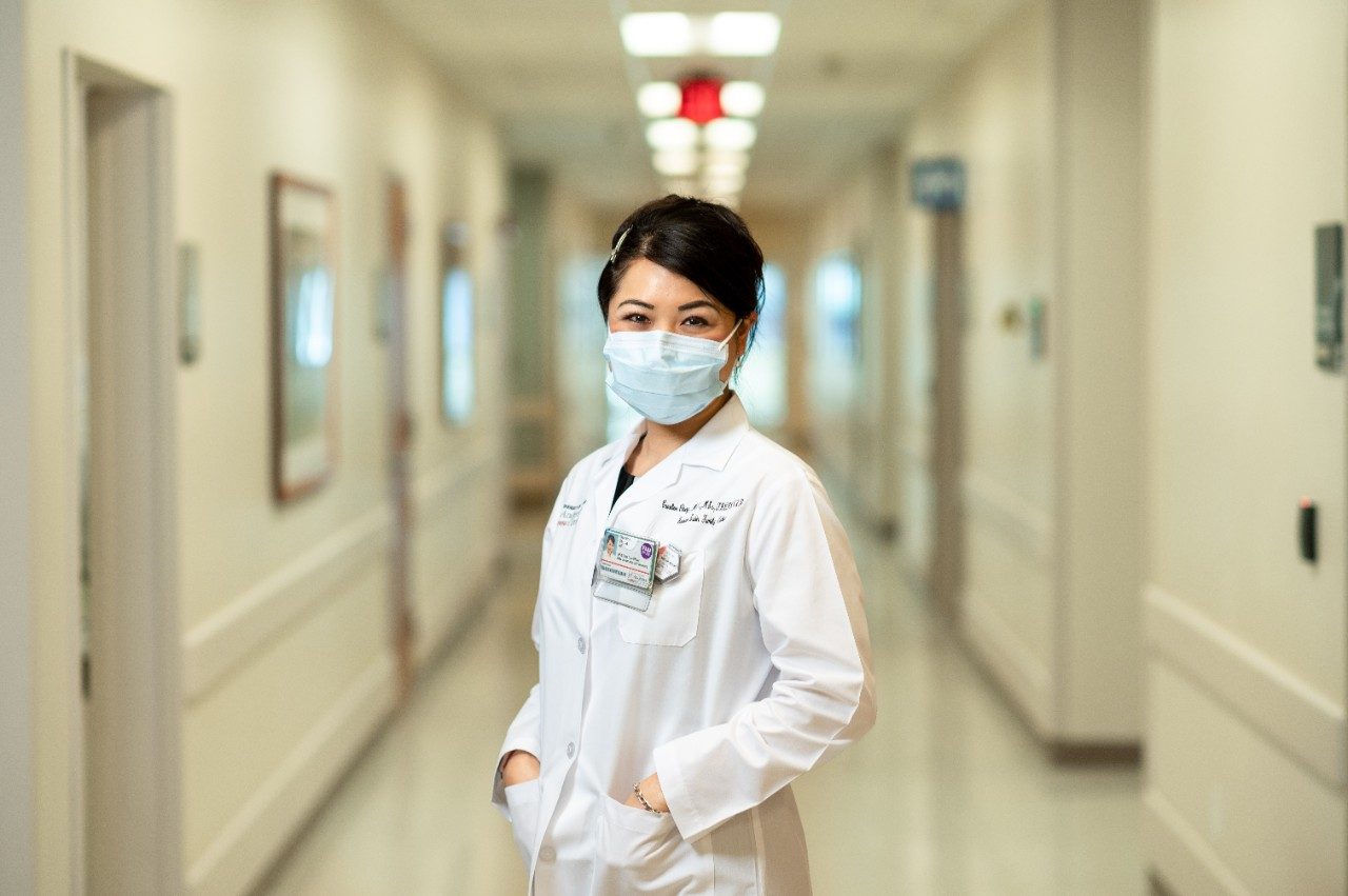 Chief Data Officer Caroline Chung, M.D., stands in the hall at MD Anderson Cancer Center while wearing a white coat and her medical-grade face mask.
