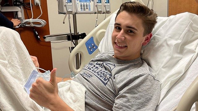 20岁的结肠直肠癌症幸存者Jaystan戴维斯,微笑,给医院的病床上的“竖起大拇指”的标志