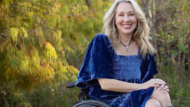 膀胱癌幸存者凯伦·罗伊（Karen Roy），坐在户外坐在轮椅上，穿着蓝色天鹅绒连衣裙
