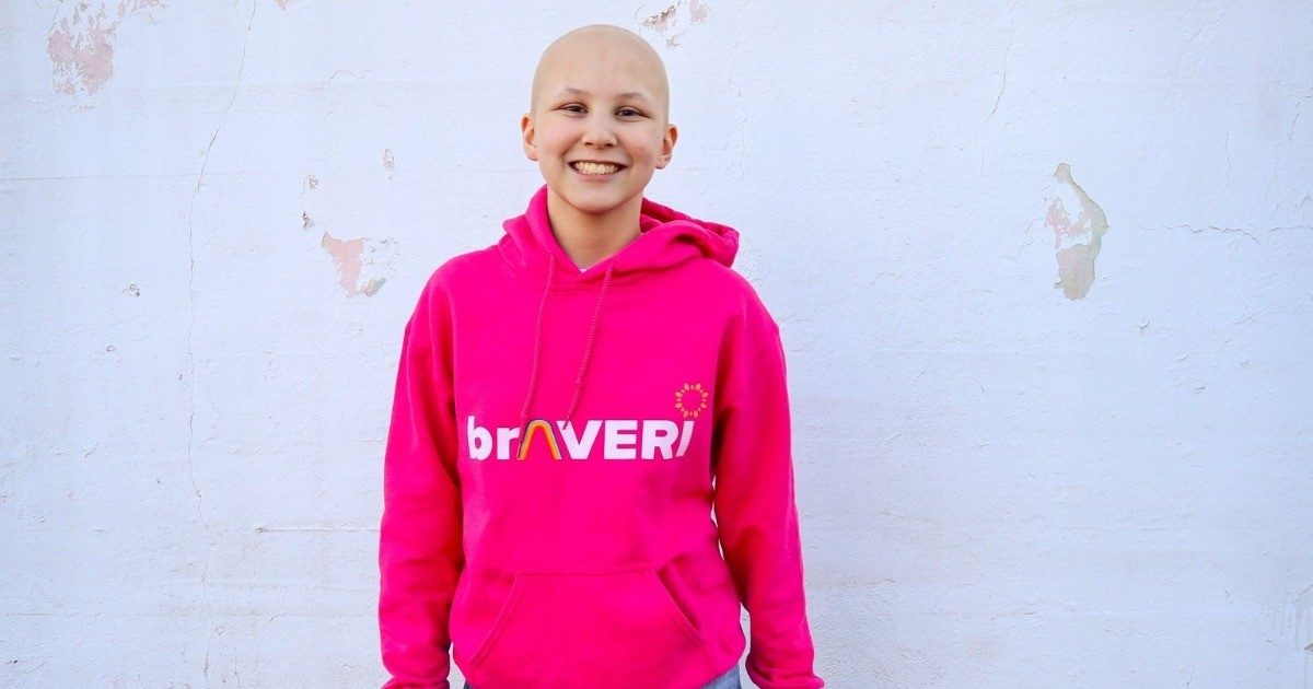 Averi布朗站在白墙前穿着粉红色运动衫与单词“braveri”。