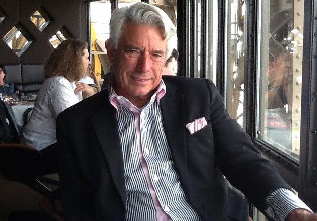 巴克马丁内斯坐在一张桌子在餐厅里穿一件黑色外套和白色的条纹衬衫。