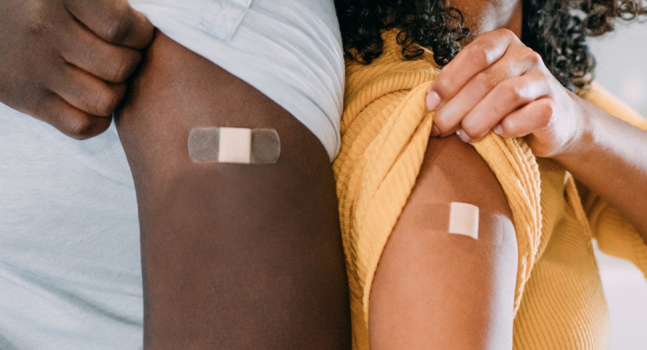 关闭-up view of two arms with sleeves rolled up and bandages covering recent vaccinations