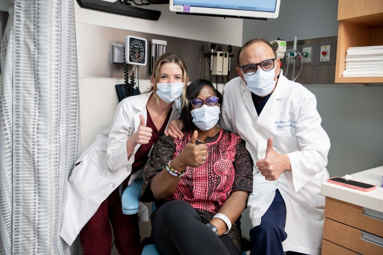 幸存者Regina吉布斯给竖起大拇指在诊所,连同Katherine heiberg医生助理(左)和Ehab汉娜,医学博士(右)