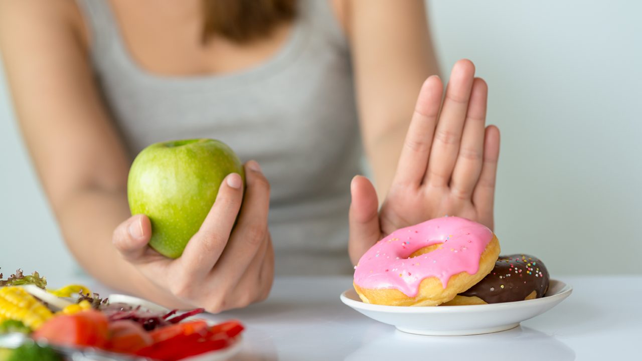一个女人一手拿着苹果，另一只手拒绝吃甜甜圈