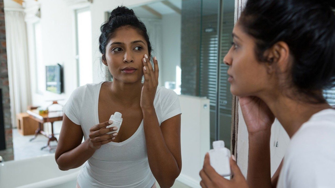 女人涂抹防晒品，以她的脸在镜子