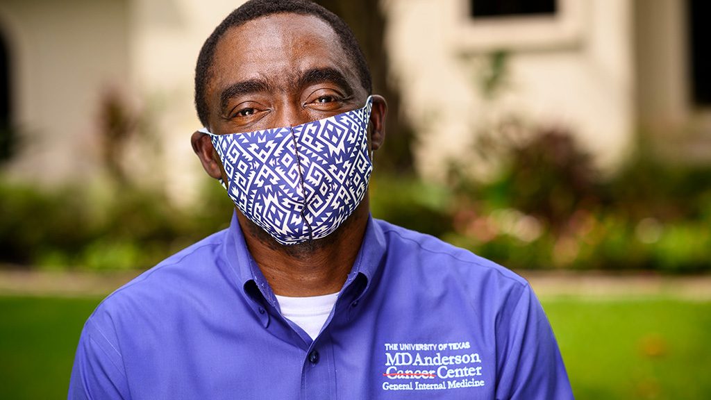 Josiah Halm，M.D.，在家里穿着蓝色和白色的布料面膜，以及他的蓝色按钮衬衫与右上角的MD安德森标志